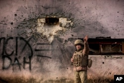 A Ukrainian serviceman points to the direction of the incoming shelling next to a building which was hit by a large caliber mortar shell in the frontline village of Krymske, Luhansk region, in eastern Ukraine, Feb. 19, 2022.