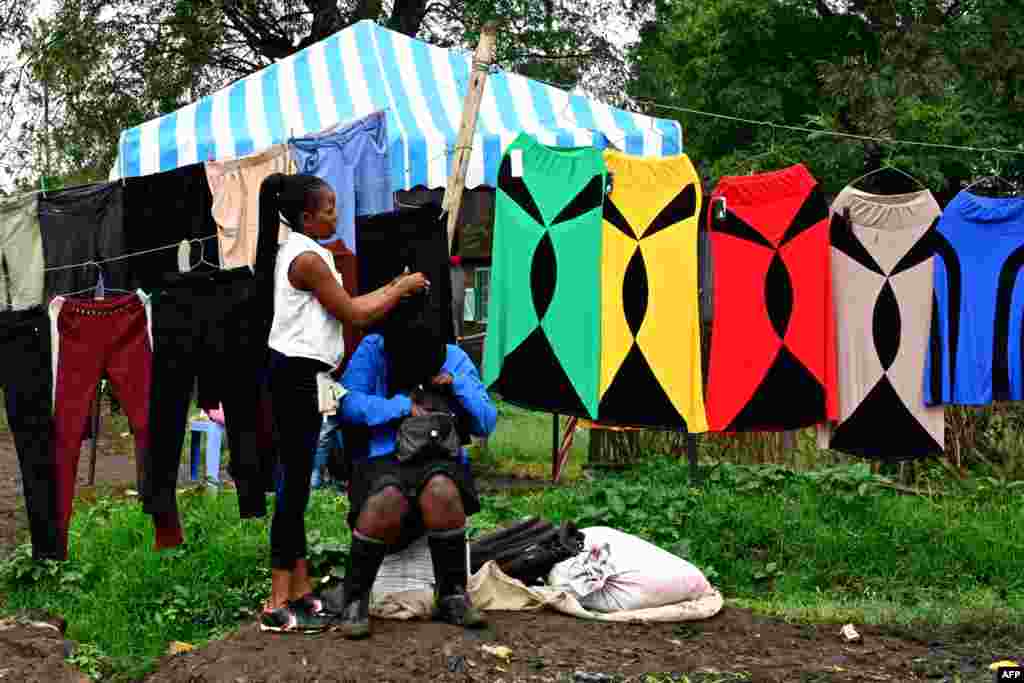 A woman plaits her friend's hair as they sell second-hand clothes in Nairobi's Makadara district, Kenya.