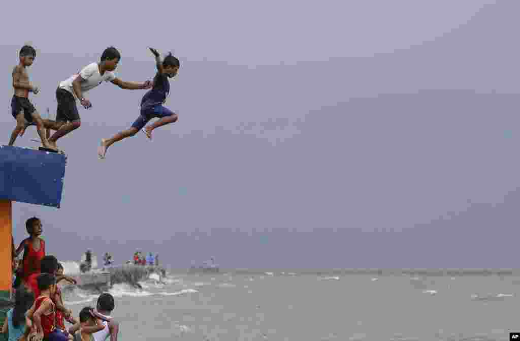 Boys jump into the water despite strong waves after a strong downpour at Manila's bay, Philippines.