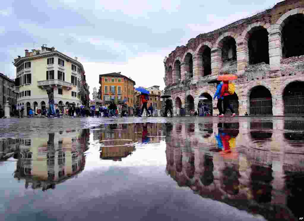 Tourists walk in the pouring rain along the old arena, right, and buildings of the old town in Verona, Italy.