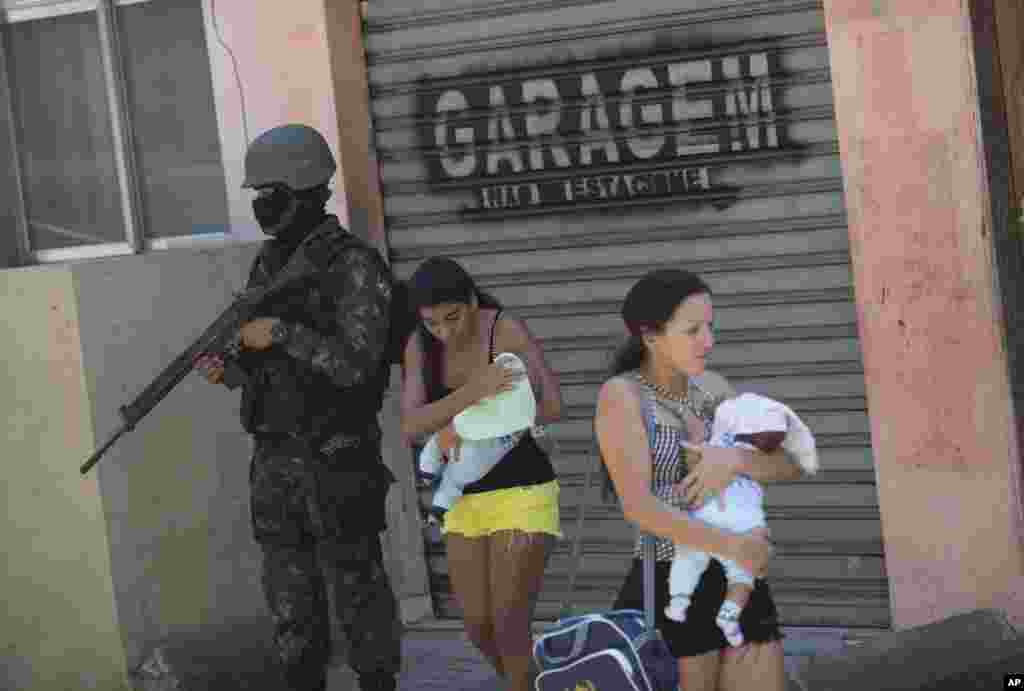Women carring their babies walk past a soldier during an operation at the Rocinha slum, in Rio de Janeiro, Brazil. More than 1,000 police and soldiers are searching Rio's largest slum for weapons and ammunition amid a crackdown on drug gangs.