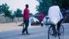 A cyclist rides past Civilian Joint Force members who are patrolling the streets looking for Boko Haram fighters. Maiduguri, Nigeria. (C. Oduah for VOA)