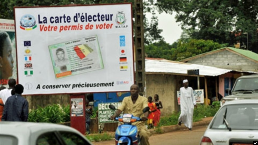People walk in front of posters for the presidential elections and instructions on the voting card, Conakry, 25 Jun 2010