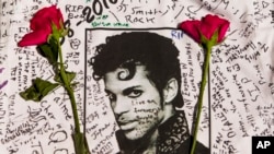 Una camiseta con la imagen de Prince y firmada por fans del fallecido cantante es enmarcada por flores dejadas por admiradores del artista en un altar creado en su honor afuera del teatro Apollo en Nueva York, el 22 de abril de 2016.