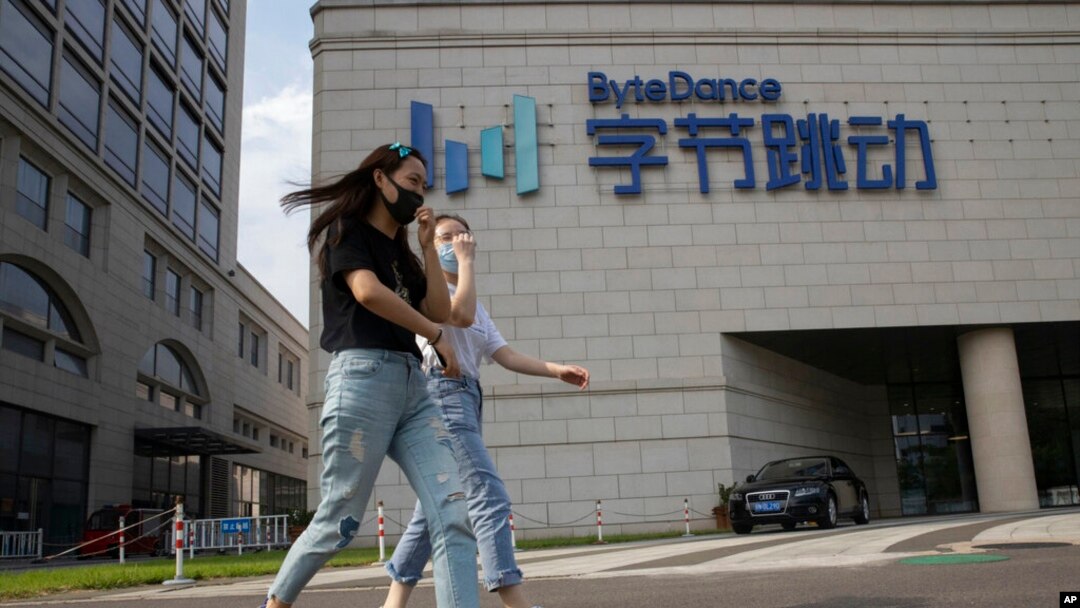 FILE - Women wearing masks to prevent the spread of the coronavirus chat as they pass by the headquarters of ByteDance, owners of TikTok, in Beijing, China, Aug. 7, 2020.