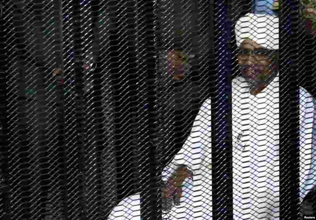 Sudan's former president Omar Hassan al-Bashir sits guarded inside a cage at the courthouse where he is facing corruption charges, in Khartoum, Aug. 19, 2019.