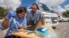 Jaqueline Goes de Jesus (Fundacao Oswaldo Cruz, Salvador), left, and Nuno Faria (University of Oxford, UK) use the Oxford Nanopore MinION device in front of the minibus equipped with a lab, in Joao Pessoa, Brazil. (Courtesy - Ricardo Funari)