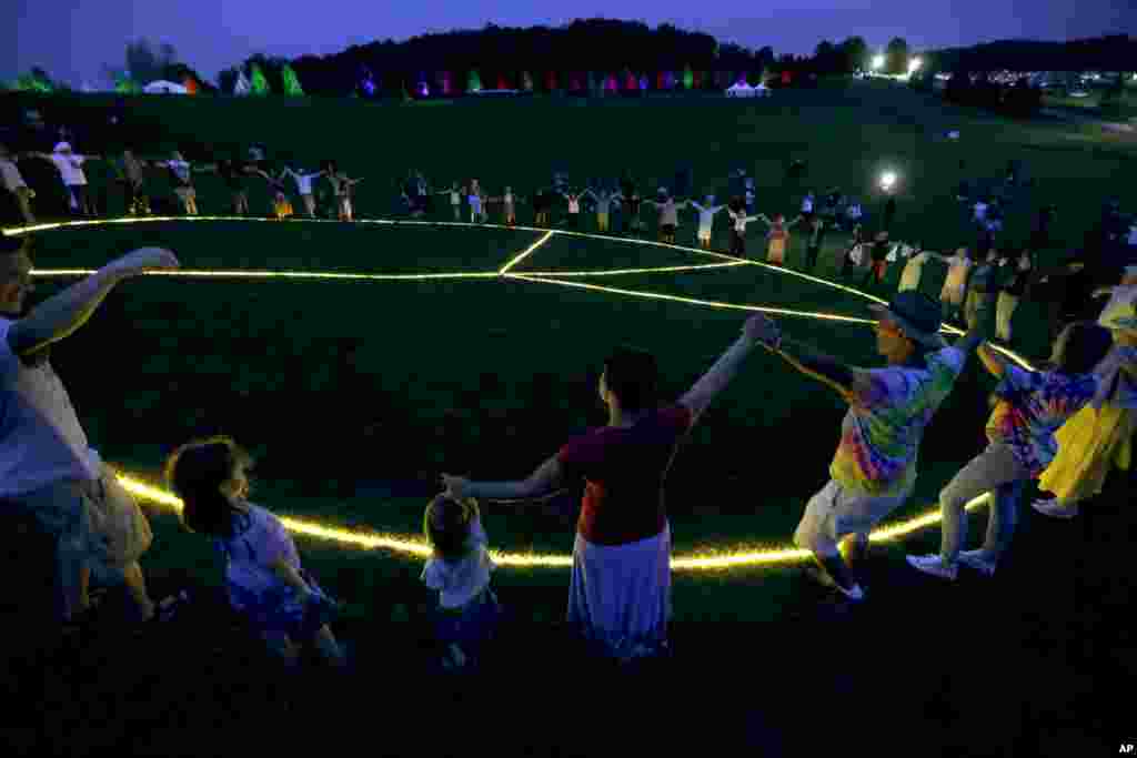 People hold hands in a circle around a large, illuminated peace sign on the original site of the 1969 Woodstock Music and Arts Fair in Bethel, N.Y., Aug. 15, 2019.