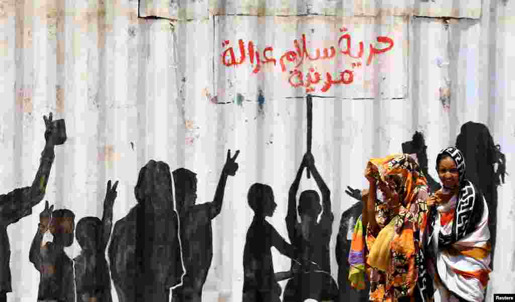 People walk past graffiti reading in Arabic "Freedom, Peace, Justice and Civilian" in the Burri district of Khartoum, Khartoum, Sudan.