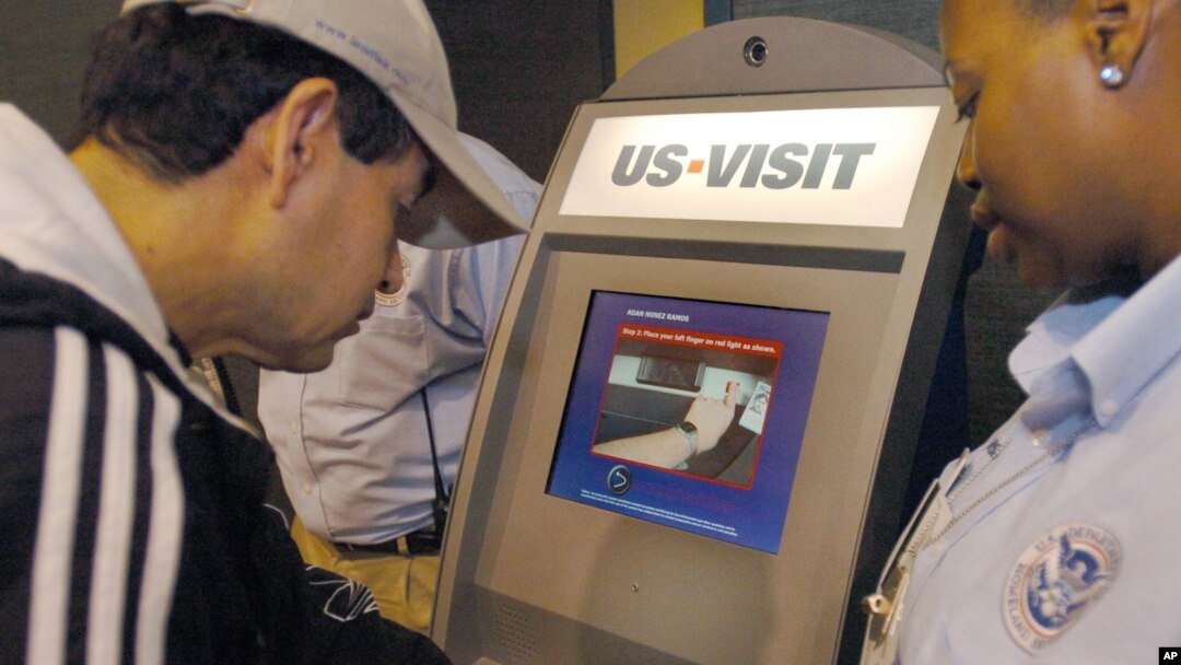 FILE - Department of Homeland Security official (r) assist a passenger (l) as he scans his fingerprint on a machine, part of the exit process at Hartsfield-Jackson Atlanta International Airport in Atlanta. The White House said the country's homeland security agency is immediately altering its electronic visa-free clearance system.