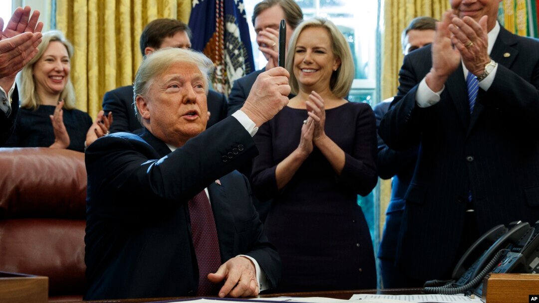 President Donald Trump holds up a pen during a signing ceremony of the "Cybersecurity and Infrastructure Security Agency Act," in the Oval Office of the White House, Nov. 16, 2018, in Washington.