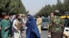 Taliban forces block the roads around the airport, while a woman with Burqa walks passes by in Kabul, on August 27, 2021. (Reuters)